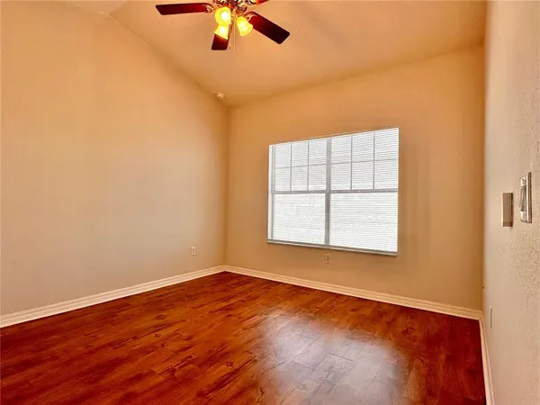 an empty room with wooden floor chandelier fan and windows