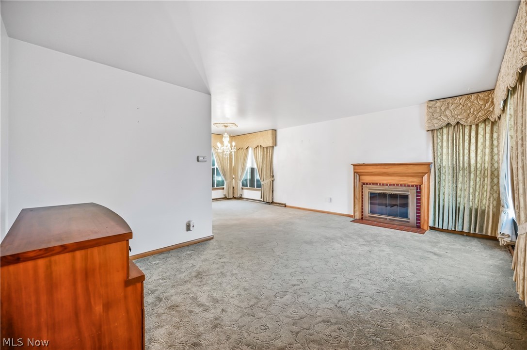 267 Butler Road Northeast Warren, OH 44483 - Photo 17 of 50 Unfurnished living room featuring a fireplace with flush hearth, light colored carpet, and a chandelier