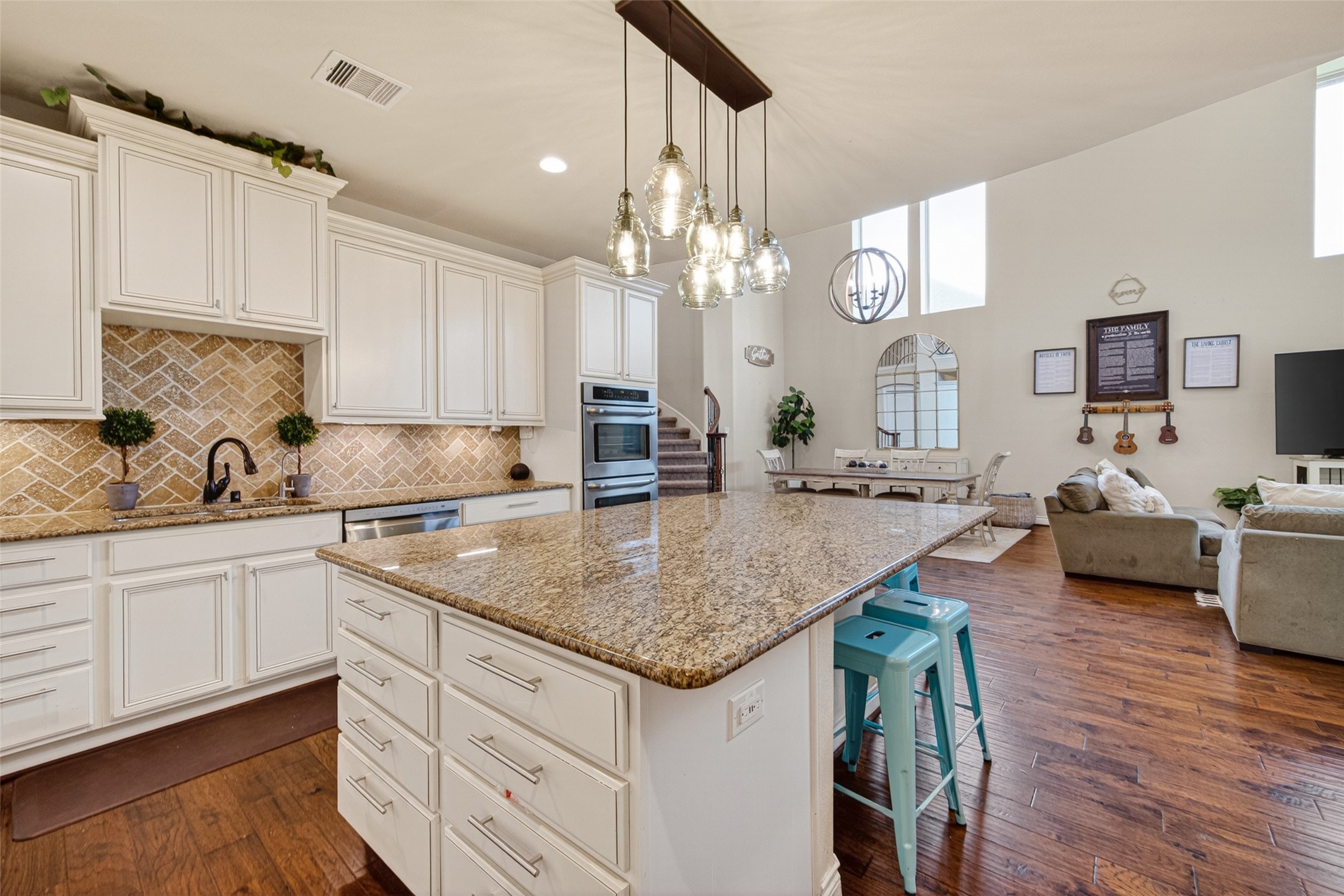 25611 Ellis Ridge Court Katy, TX 77494 - Photo 17 of 49 This spacious open-concept kitchen and living area features elegant white cabinetry, a large granite island with bar seating, and stylish pendant lighting. The room is bright and inviting with high ceilings, hardwood floors, and a cozy living space. Perfect for entertaining and family gatherings.