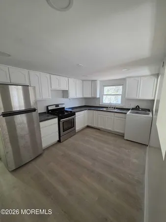 a large white kitchen with stainless steel appliances granite countertop a stove a sink a refrigerator and white cabinets
