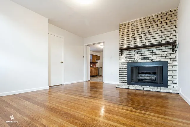 a view of an empty room with wooden floor fireplace and a window