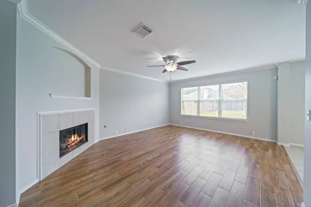 a view of an empty room with wooden floor fireplace and a window