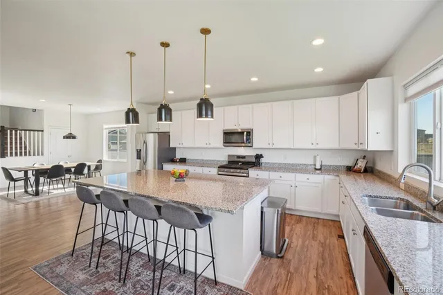 a kitchen with stainless steel appliances granite countertop a stove top oven a sink a dining table and chairs with wooden floor