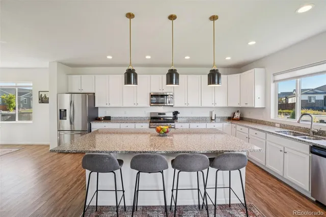 a kitchen with stainless steel appliances granite countertop a stove top oven a sink dishwasher and a refrigerator with wooden floor