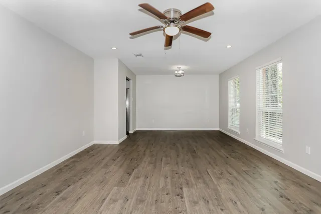 an empty room with wooden floor fan and windows