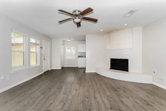 an empty room with wooden floor a ceiling fan and windows