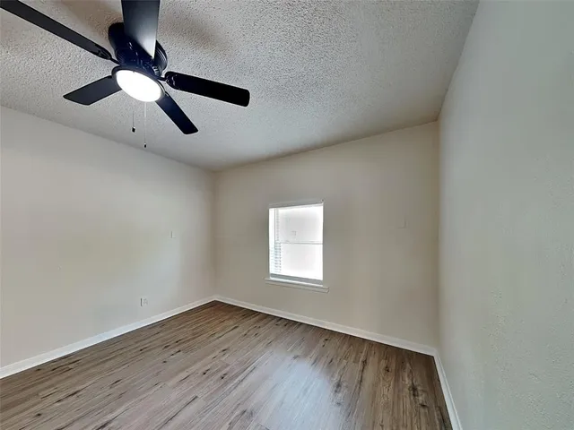 an empty room with wooden floor ceiling fan and window