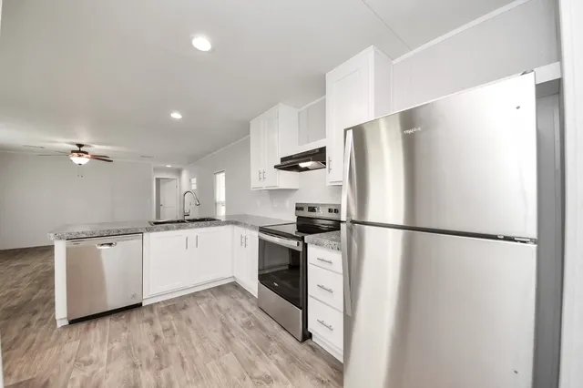 a kitchen with stainless steel appliances a refrigerator a sink and white cabinets