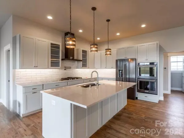 a kitchen with stainless steel appliances granite countertop a sink a stove and a wooden floor