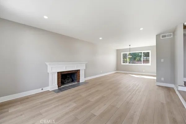 an empty room with wooden floor fireplace and windows