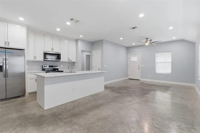 a kitchen with granite countertop a refrigerator oven a sink a window and white cabinets