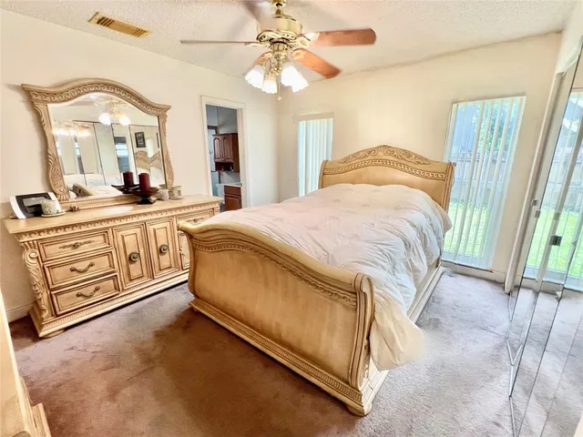 a spacious bedroom with a bed a mirror on dresser and a chandelier