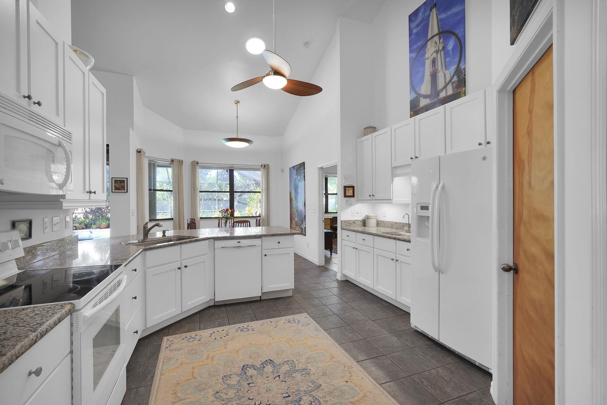 3372 Kings Road South St. Augustine, FL 32086 - Photo 11 of 48 a large white kitchen with stainless steel appliances granite countertop a stove a sink dishwasher and white cabinets with wooden floor