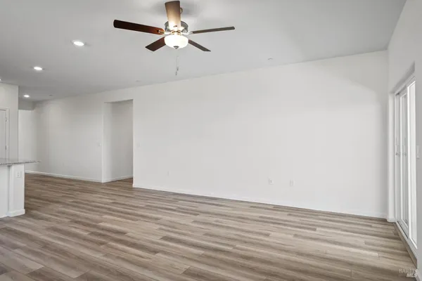 a view of an empty room with wooden floor and a ceiling fan