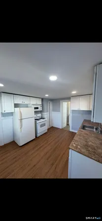 a view of kitchen and empty room with wooden floor