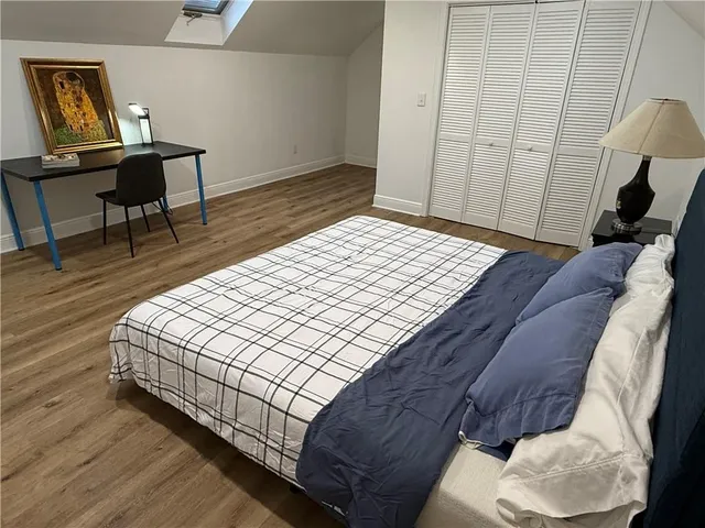 a bedroom with a bed a chair and a potted plant on the wooden floor