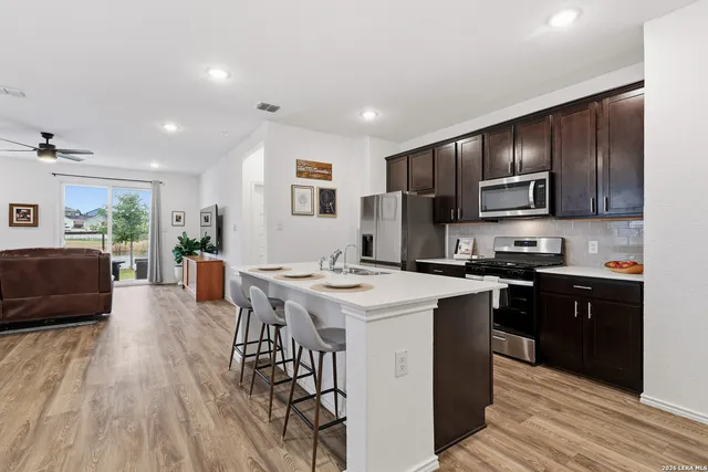 a kitchen with stainless steel appliances granite countertop a stove top oven a refrigerator a sink dishwasher and a dining table with wooden floor