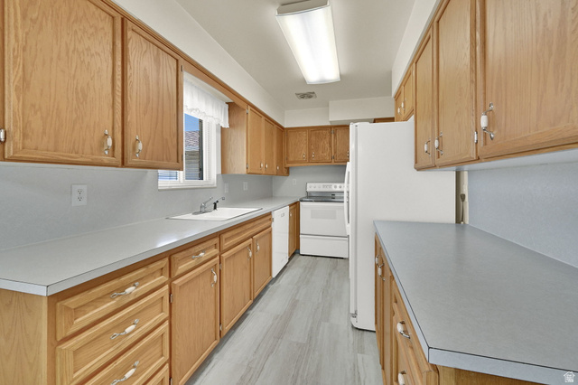 2467 South 2000 West Syracuse, UT 84075 - Photo 17 of 28 Galley kitchen featuring wood cabinetry, light countertops, wood-finish flooring, white appliances, and a window above the sink