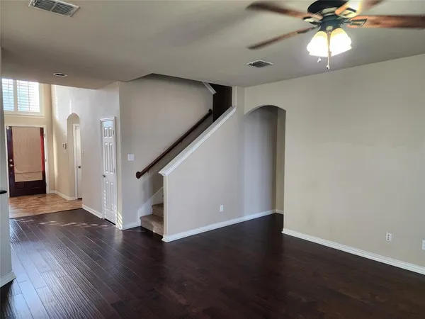 a view of an empty room with wooden floor and a ceiling fan