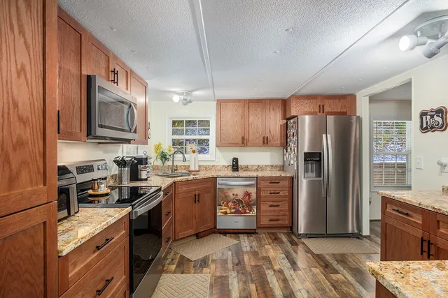 a kitchen with stainless steel appliances granite countertop a stove top oven a sink dishwasher a refrigerator and cabinets with wooden floor