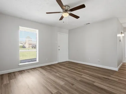 an empty room with wooden floor ceiling fan and windows