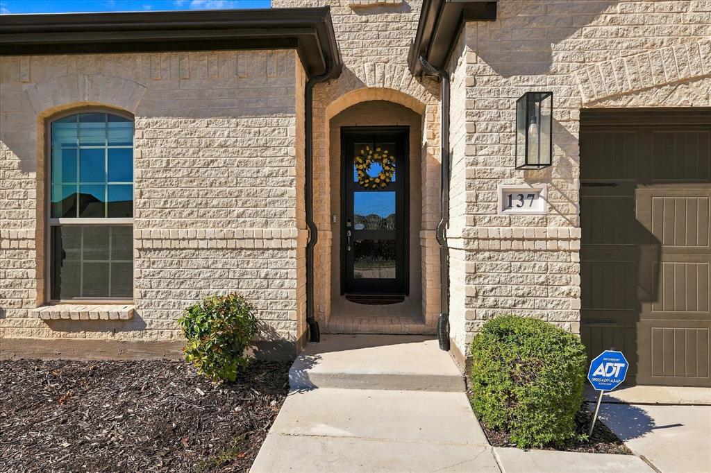 137 Chisos Court Rhome, TX 76078 - Photo 2 of 40 Light-colored brick exterior with arched entryway and a contrasting dark paneled garage door