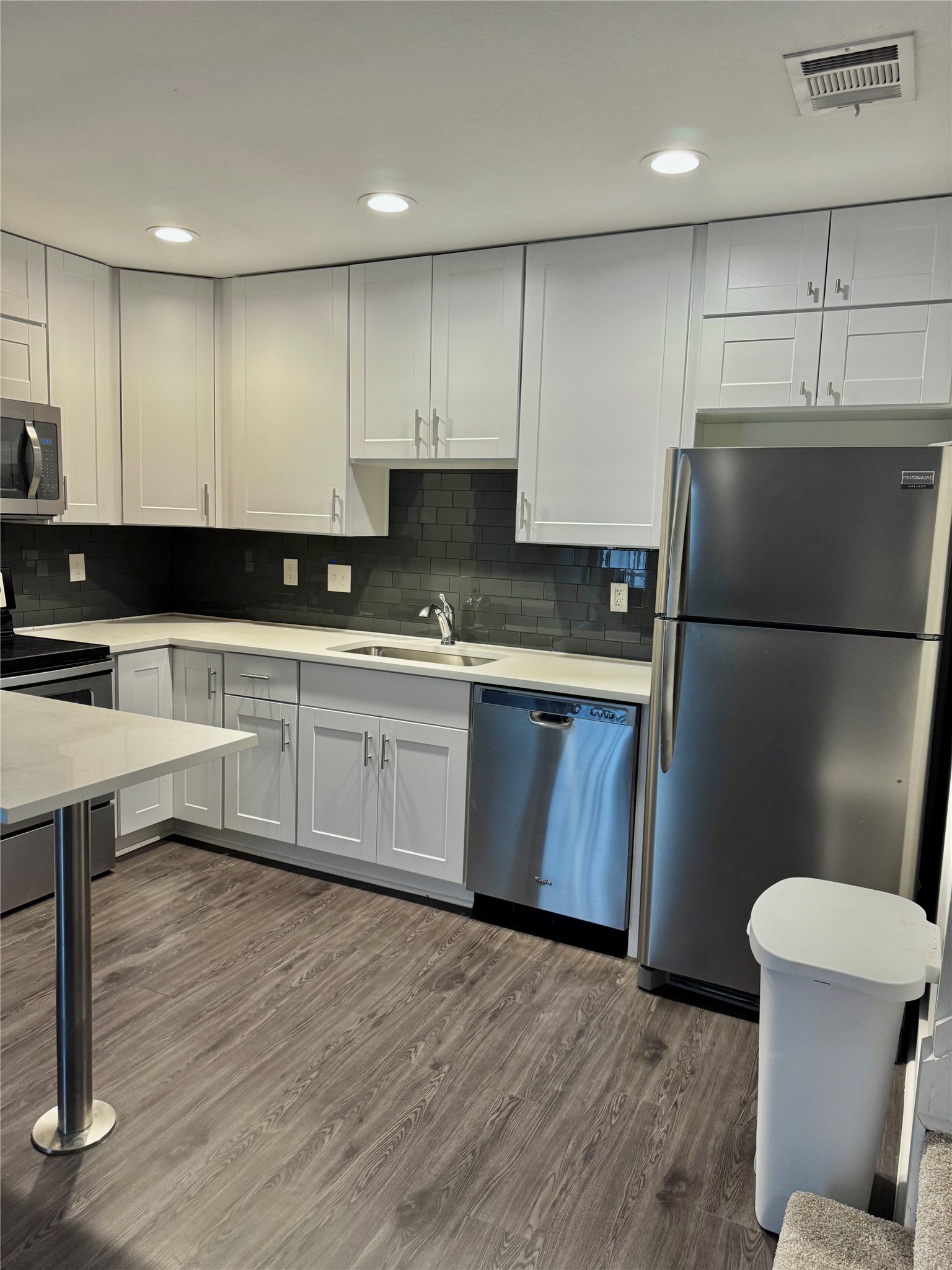 935 La Posada Drive, Unit 252 Austin, TX 78752 - Photo 6 of 20 a kitchen with a sink a refrigerator a stove and white cabinets with wooden floor