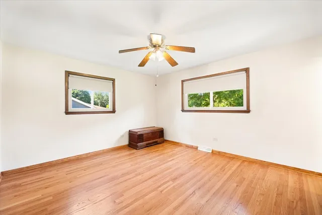 a big room with wooden floor ceiling fan and windows
