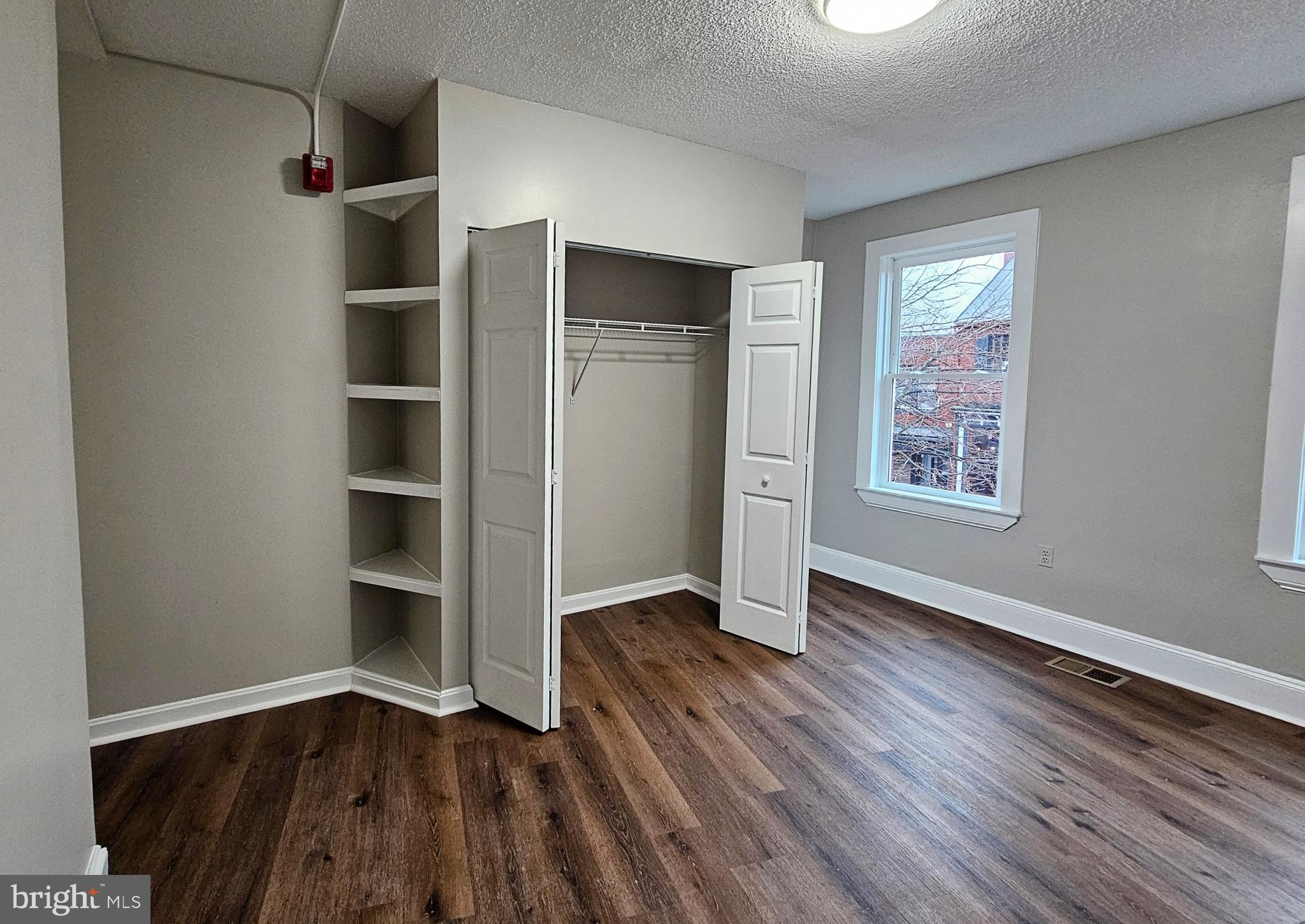 an empty room with wooden floor closet and windows