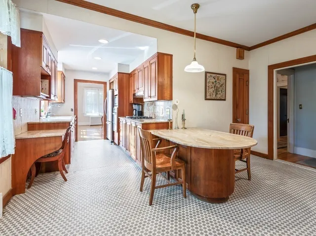 a dining hall with stainless steel appliances kitchen island granite countertop a dining table chairs and a refrigerator