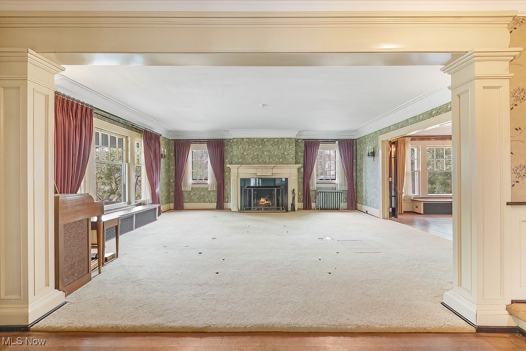 245 Merriman Road Akron, OH 44303 - Photo 15 of 49 Unfurnished living room featuring ornamental molding, wallpapered walls, a warm lit fireplace, carpet flooring, and decorative columns