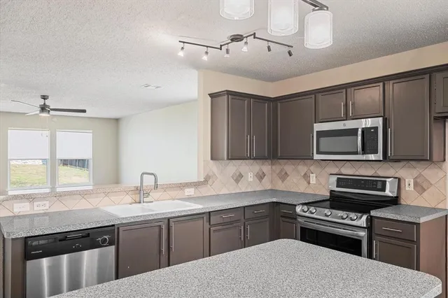 a kitchen with stainless steel appliances granite countertop a sink dishwasher a stove and a microwave oven with cabinets