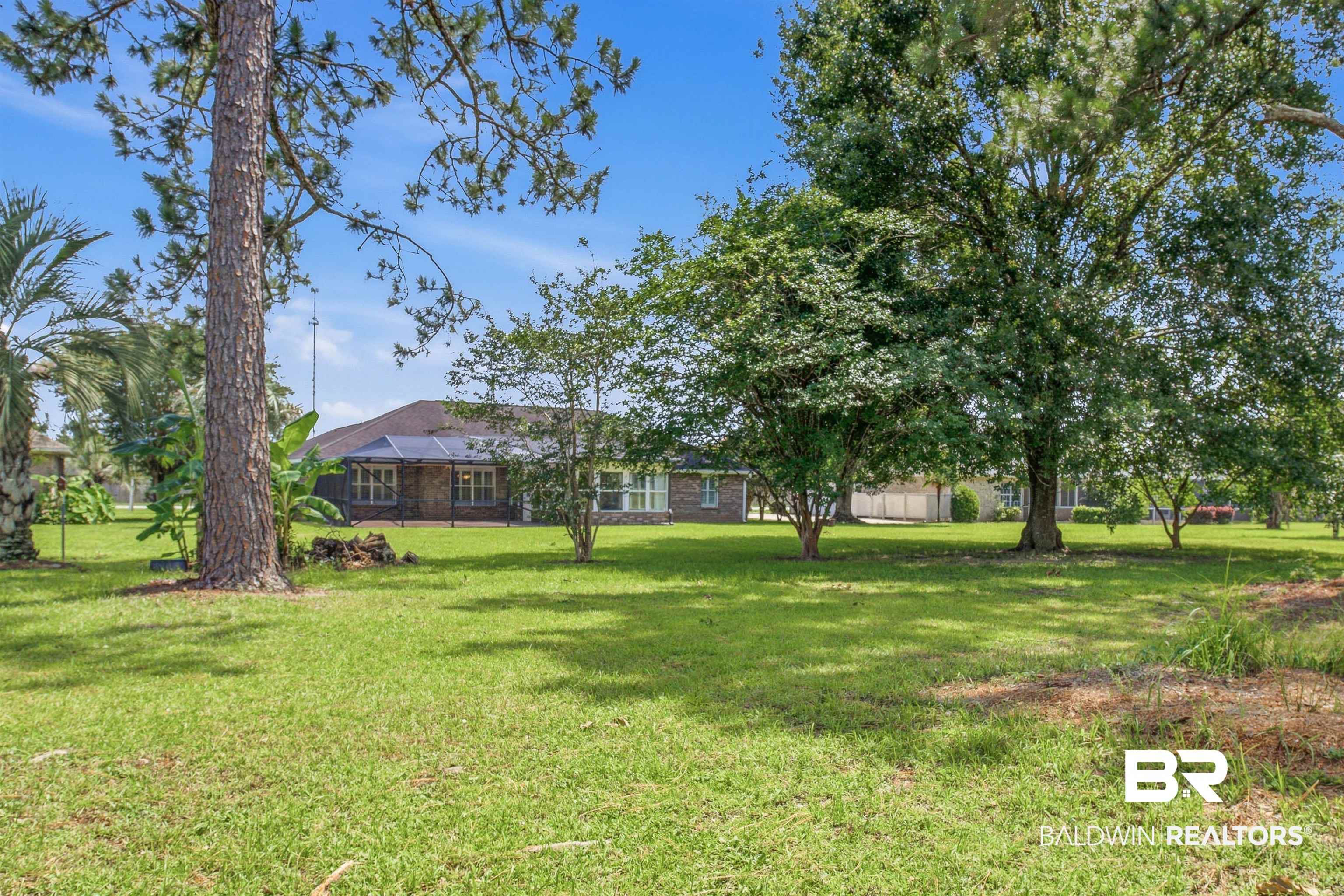 22685 County Road 12 Foley, AL 36535 - Photo 15 of 89 Expansive green lawn with mature trees and a brick-sided residence with multiple windows and a dark roofline