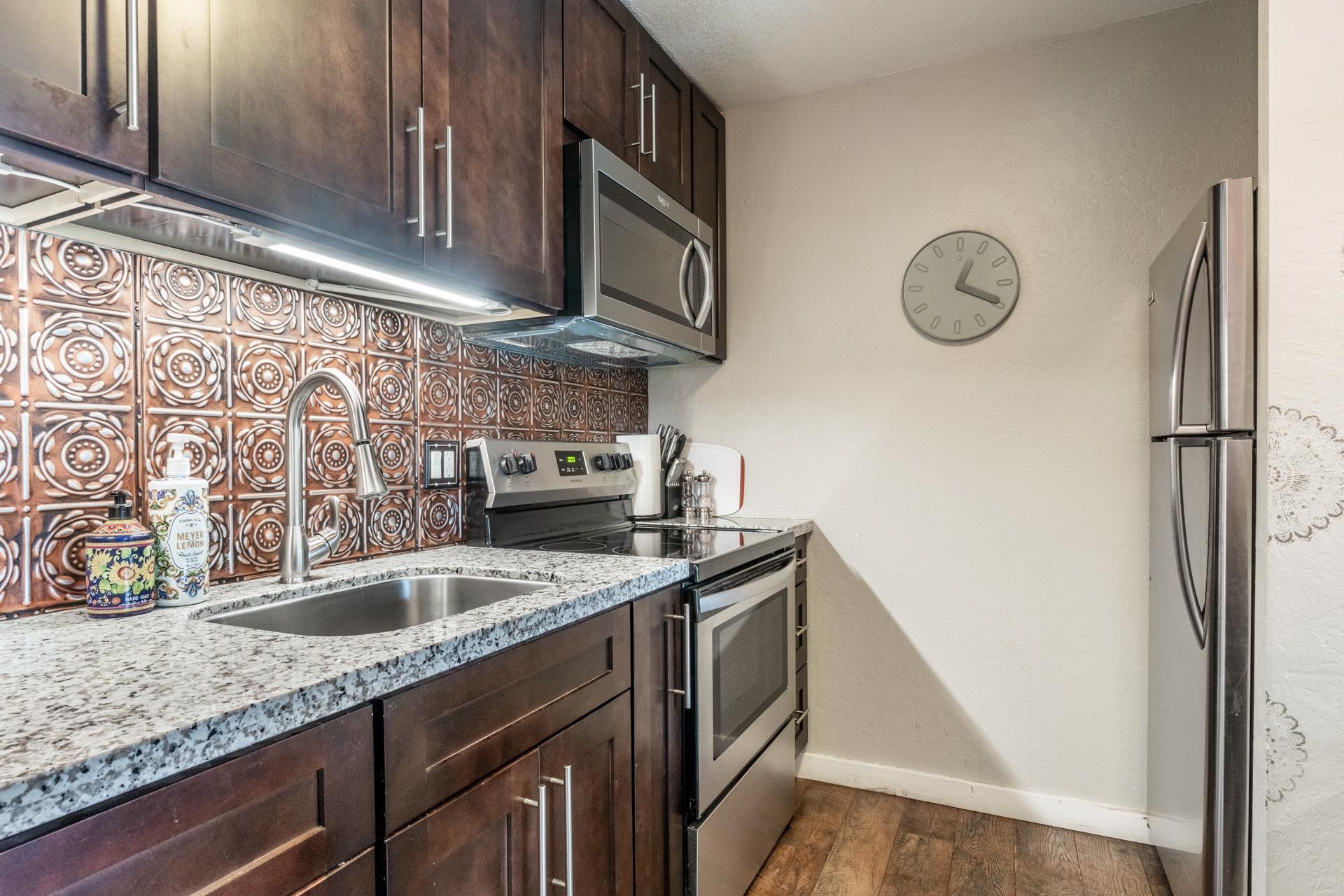2289 Sierra Nevada Road, Unit F3 Mammoth Lakes, CA 93546 - Photo 10 of 17 Kitchen with appliances with stainless steel finishes, decorative backsplash, dark brown cabinetry, dark wood-type flooring, and light stone counters