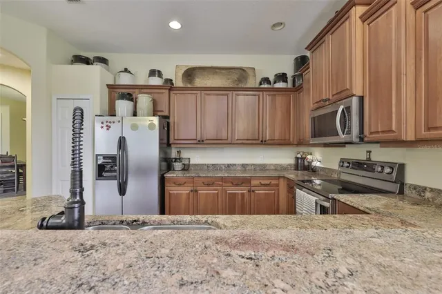 a kitchen with stainless steel appliances granite countertop a refrigerator a stove and a sink with wooden cabinets