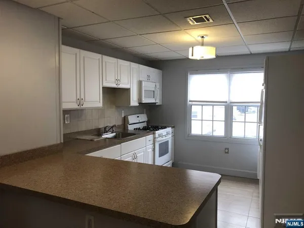 a kitchen with granite countertop a stove a sink a refrigerator and white cabinets with wooden floor