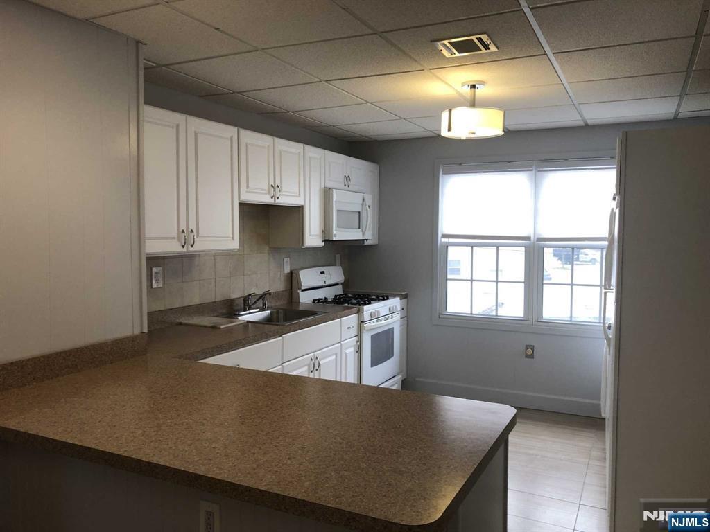 196 Rock Road, Unit 2B Glen Rock, NJ 07452 - Photo 7 of 22 a kitchen with granite countertop a stove a sink a refrigerator and white cabinets with wooden floor