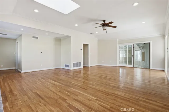 an empty room with wooden floor ceiling fan and windows
