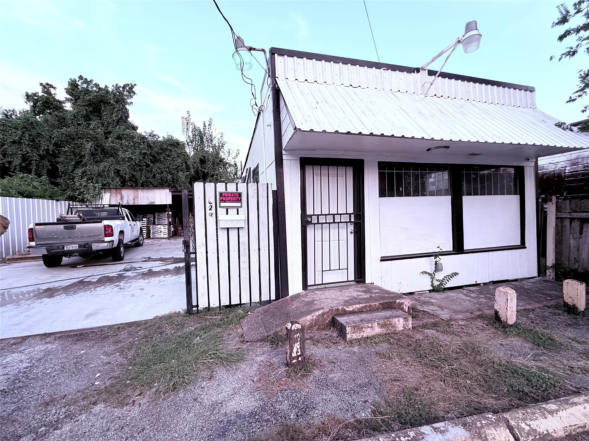 6325 Cullen Boulevard Houston, TX 77021 - Photo 1 of 18 Small, single-story building with a metal roof and a gated entrance. There's a driveway leading to a parking area with a truck. The property is fenced and bordered by trees, offering privacy. Suitable for a compact home or business.