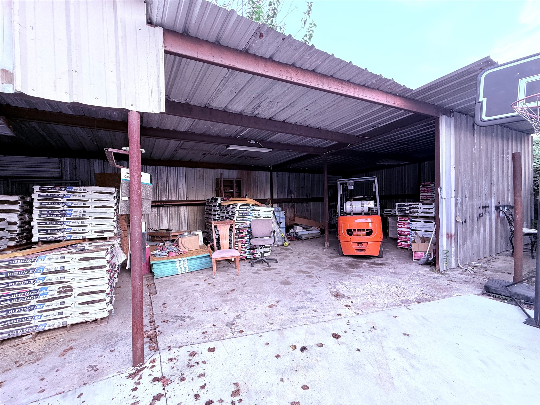 6325 Cullen Boulevard Houston, TX 77021 - Photo 15 of 18 This photo shows a spacious metal storage shed with a concrete floor. It contains various materials, a forklift, and a basketball hoop mounted outside. Ideal for extra storage or workshop use.