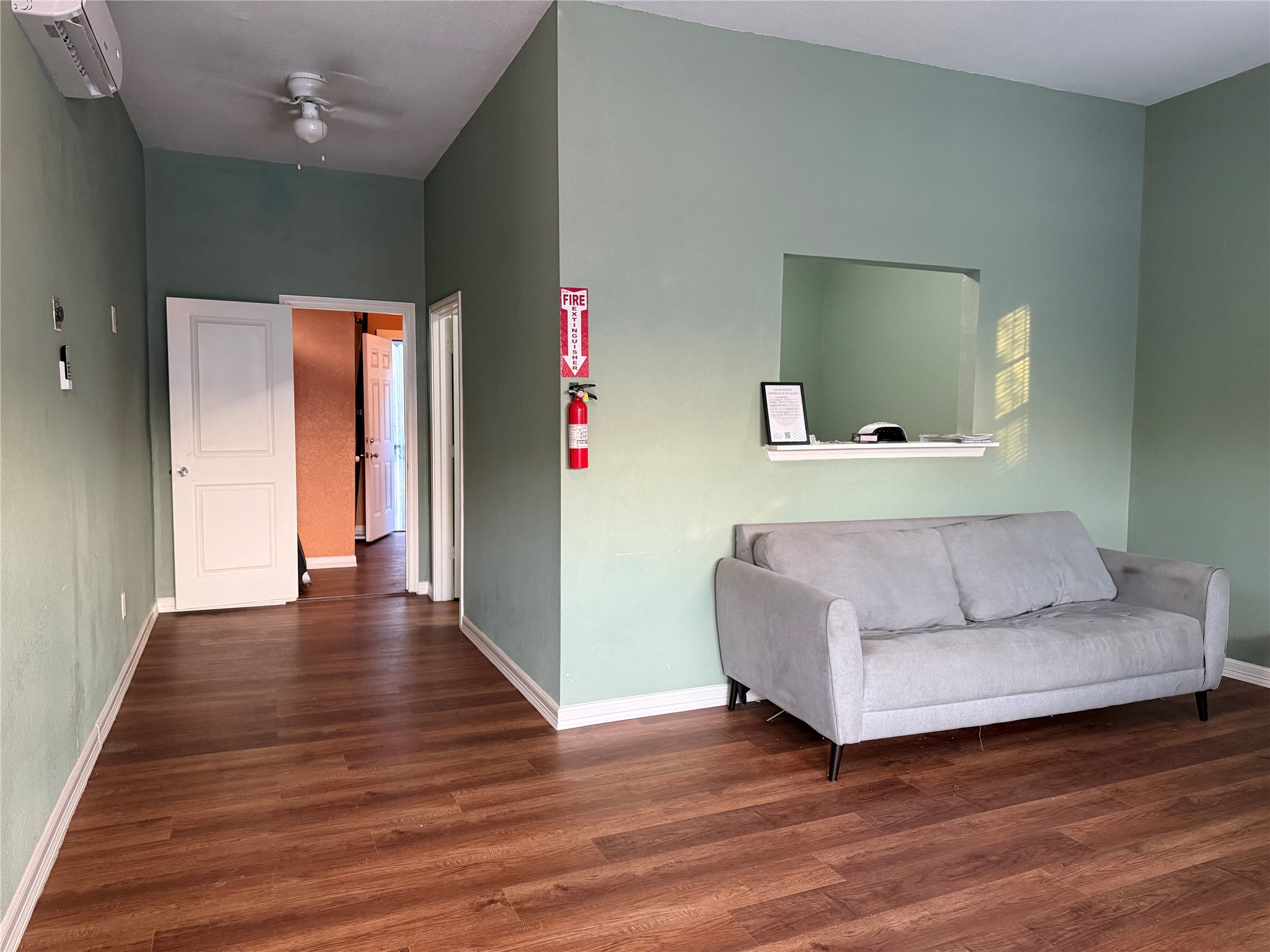 6325 Cullen Boulevard Houston, TX 77021 - Photo 4 of 18 This room features a cozy layout with light green walls, a ceiling fan, and wood flooring. It includes a comfortable gray sofa and a pass-through window. The space is well-lit with natural light and has easy access to adjacent rooms.