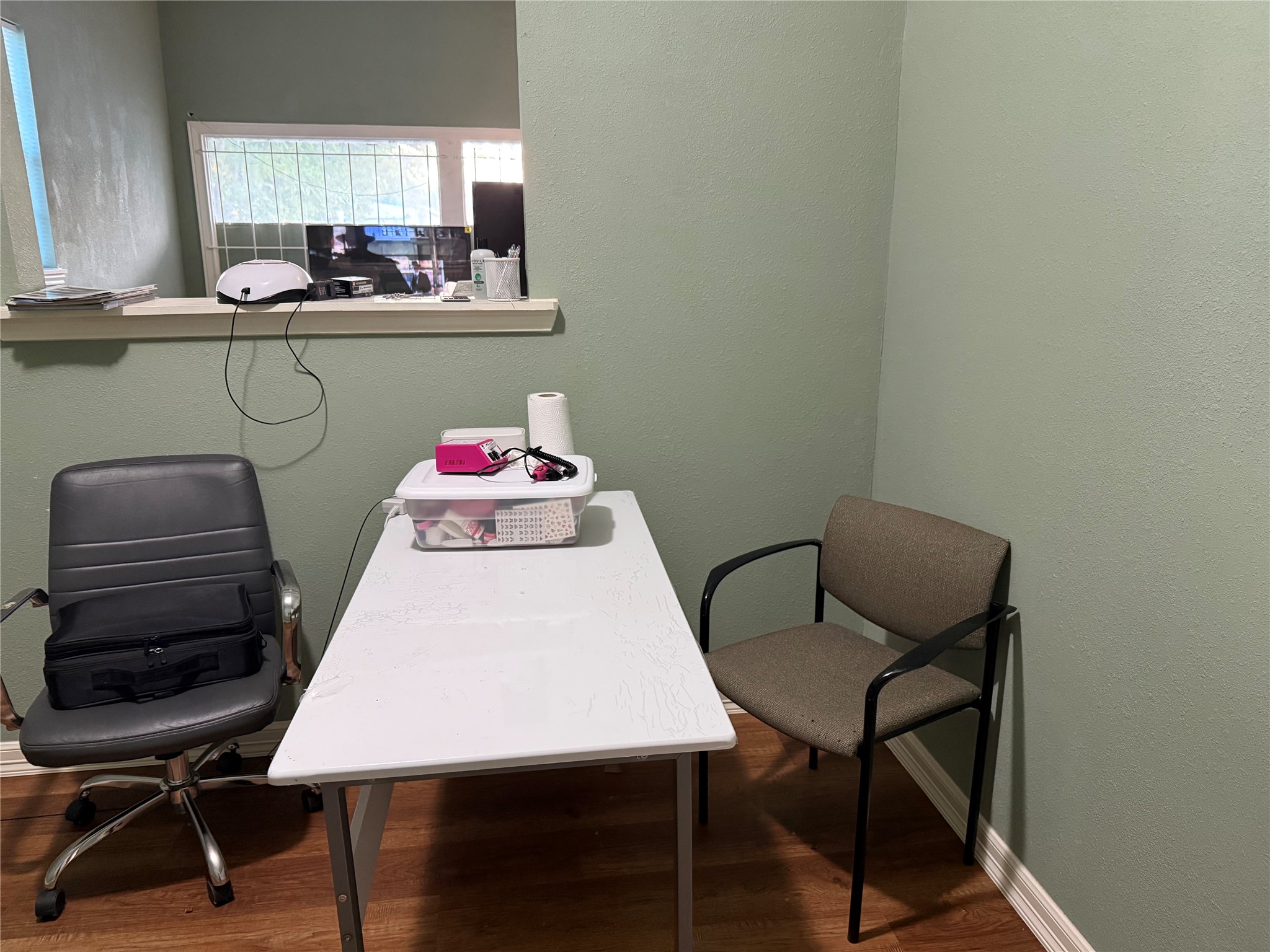 6325 Cullen Boulevard Houston, TX 77021 - Photo 7 of 18 This small room features light green walls and wood flooring, furnished with a white table and two chairs. A high interior window offers a view into the adjacent space, providing natural light. Ideal for a compact office or study area.