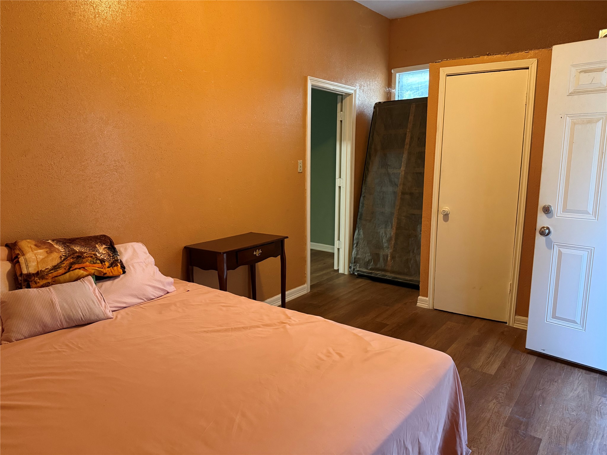 6325 Cullen Boulevard Houston, TX 77021 - Photo 9 of 18 This room features warm, orange-toned walls with wood flooring. It includes a bed with a side table, a closet, and an additional door leading to another space. A small window provides some natural light.