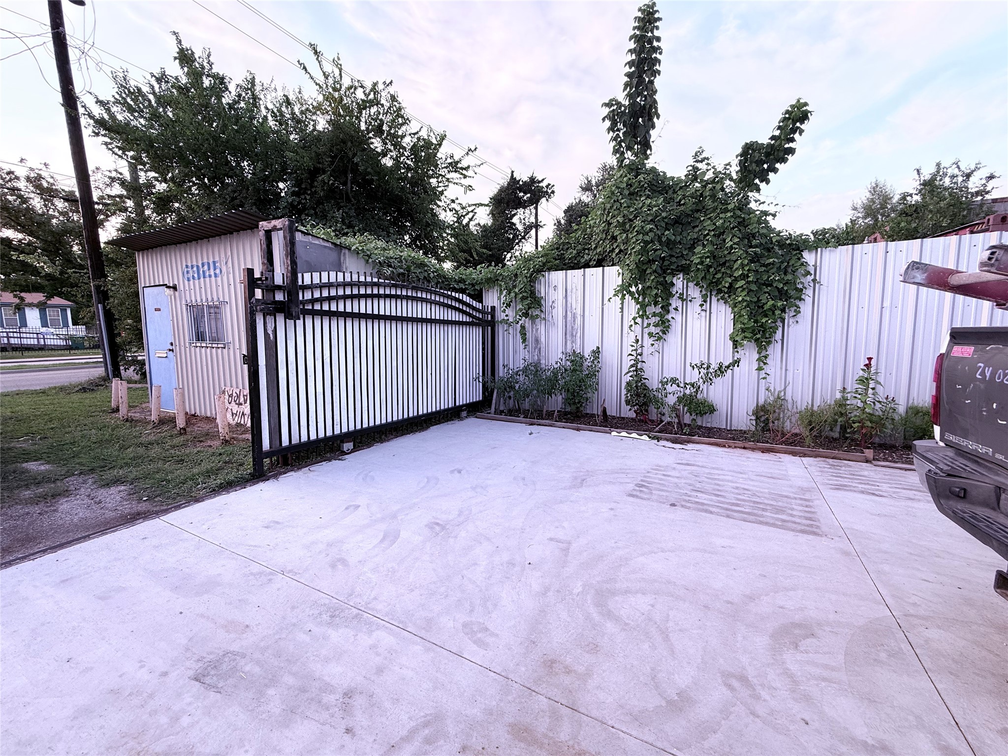 6325 Cullen Boulevard Houston, TX 77021 - Photo 10 of 18 This photo shows a paved driveway with a metal gate, adjacent to a small shed. The area is bordered by a white corrugated fence covered with greenery, providing privacy and a touch of nature.