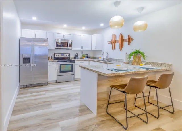 a kitchen with stainless steel appliances granite countertop a stove a refrigerator a sink a dining table and chairs with wooden floor