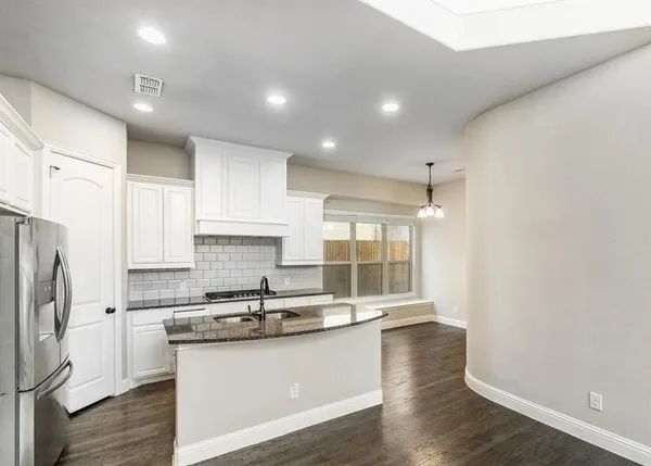 a kitchen with stainless steel appliances granite countertop a refrigerator a sink a stove a microwave and white cabinets with wooden floor