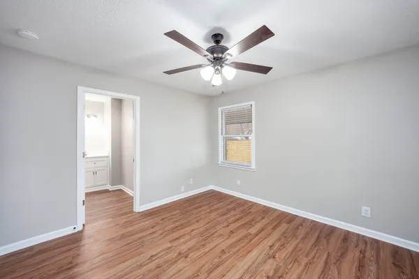 an empty room with wooden floor ceiling fan and windows
