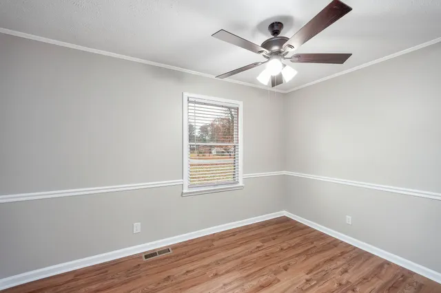 an empty room with wooden floor fan and windows