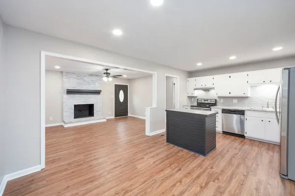 a large kitchen with kitchen island a sink dishwasher a refrigerator and white cabinets with wooden floor