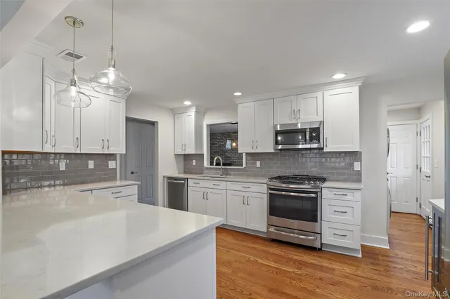 a kitchen with stainless steel appliances granite countertop a stove top oven a sink dishwasher a refrigerator and white cabinets with wooden floor